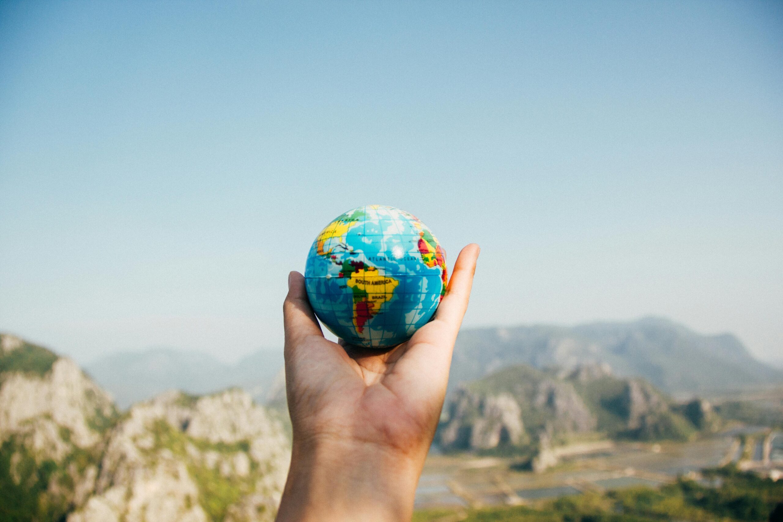 Home Hand holding a globe against a mountain background symbolizing travel and exploration.